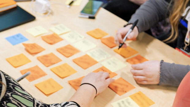 post-it notes laid out on a table, with two people's hands visible adding some new notes